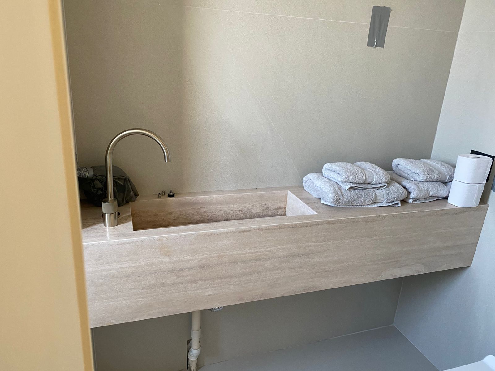 Lavabo com bancada suspensa em travertino e cuba retangular esculpida