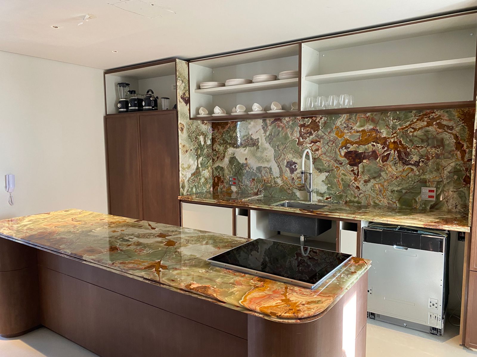 Cozinha com ilha em ônix verde, cooktop embutido e painel de fundo na mesma pedra