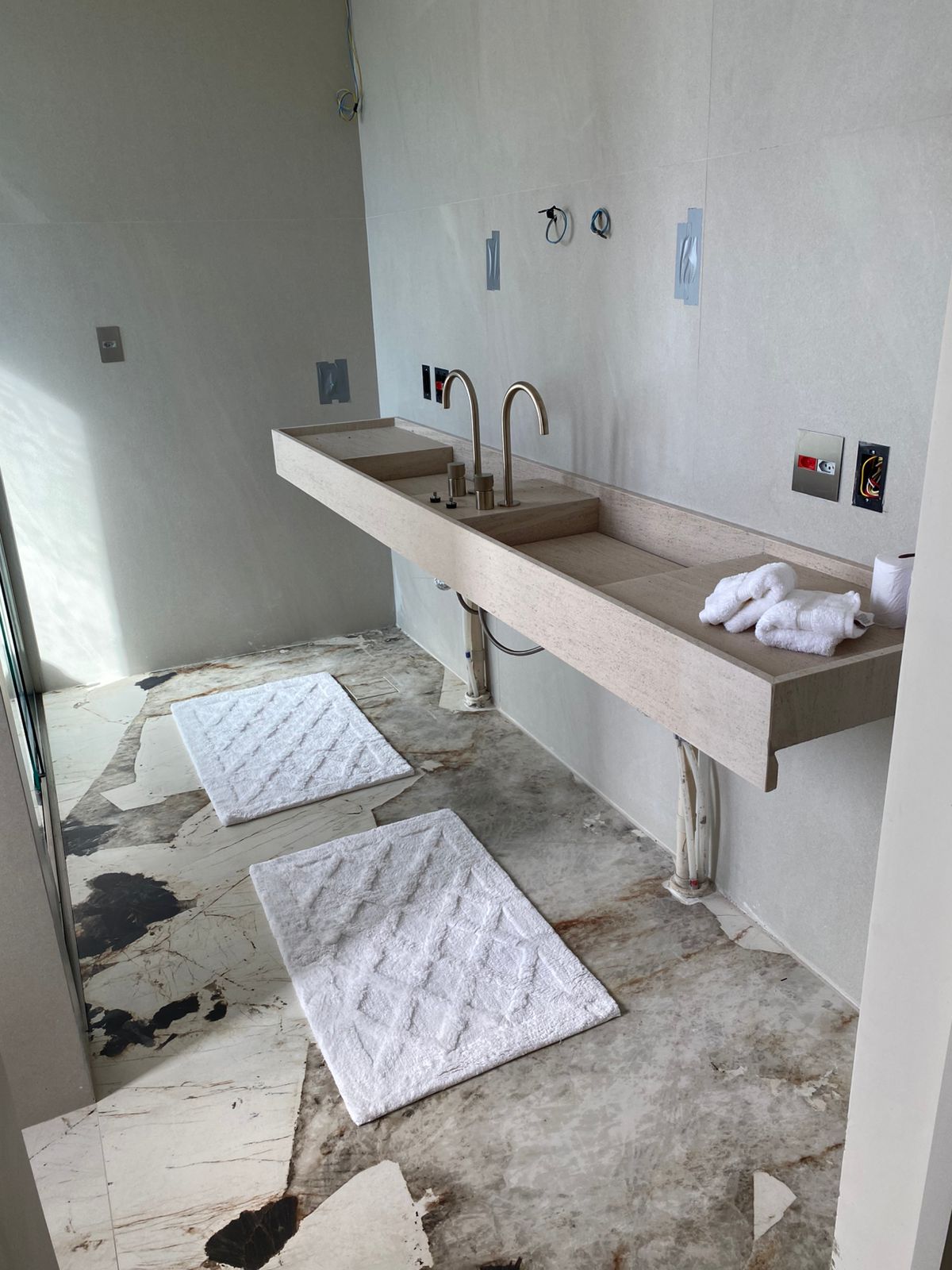 Banheiro com bancada suspensa em travertino, cuba esculpida e piso em quartzito