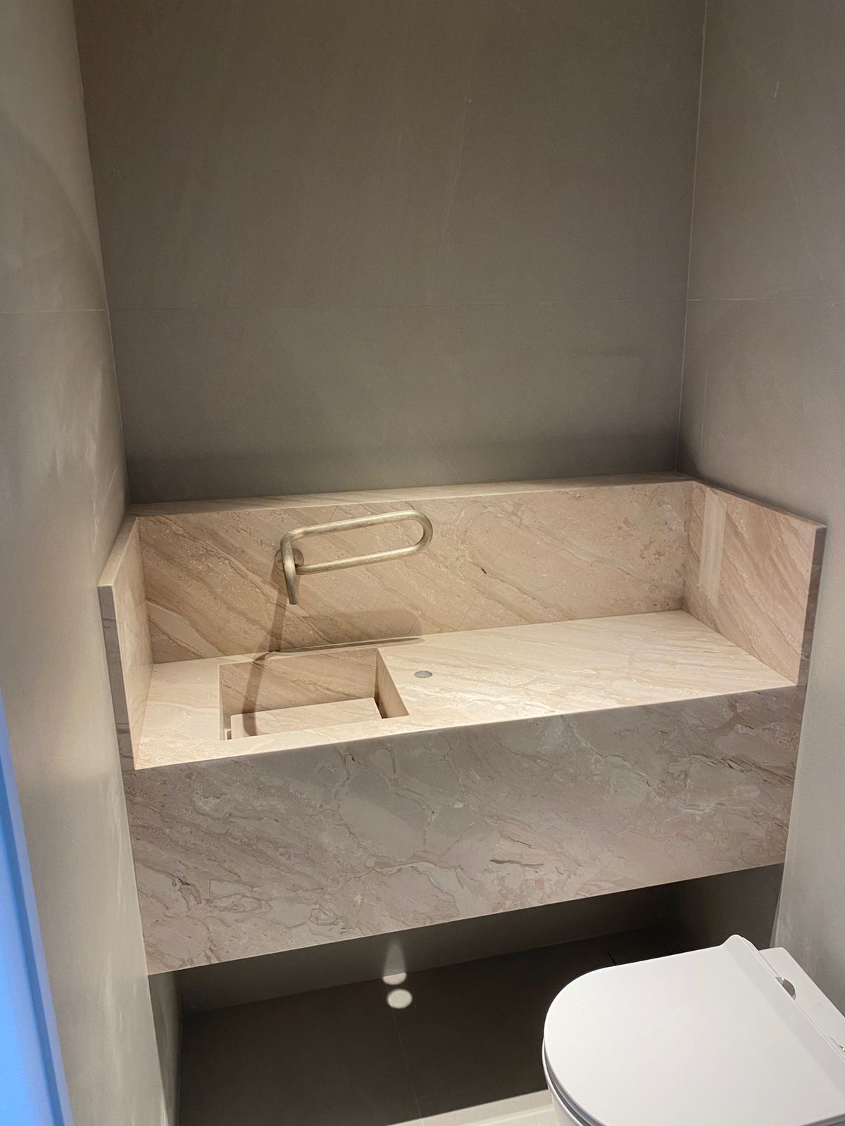 Lavabo em travertino bege com rodabanca alta, cuba esculpida e torneira de parede
